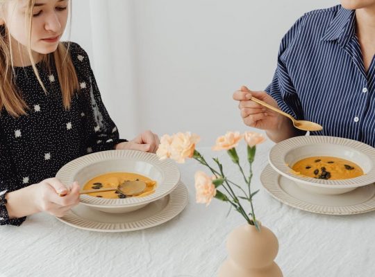 Two women enjoying homemade pumpkin soup at a dining table with floral decor.