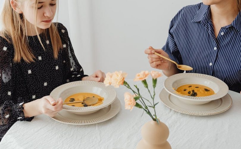 Two women enjoying homemade pumpkin soup at a dining table with floral decor.